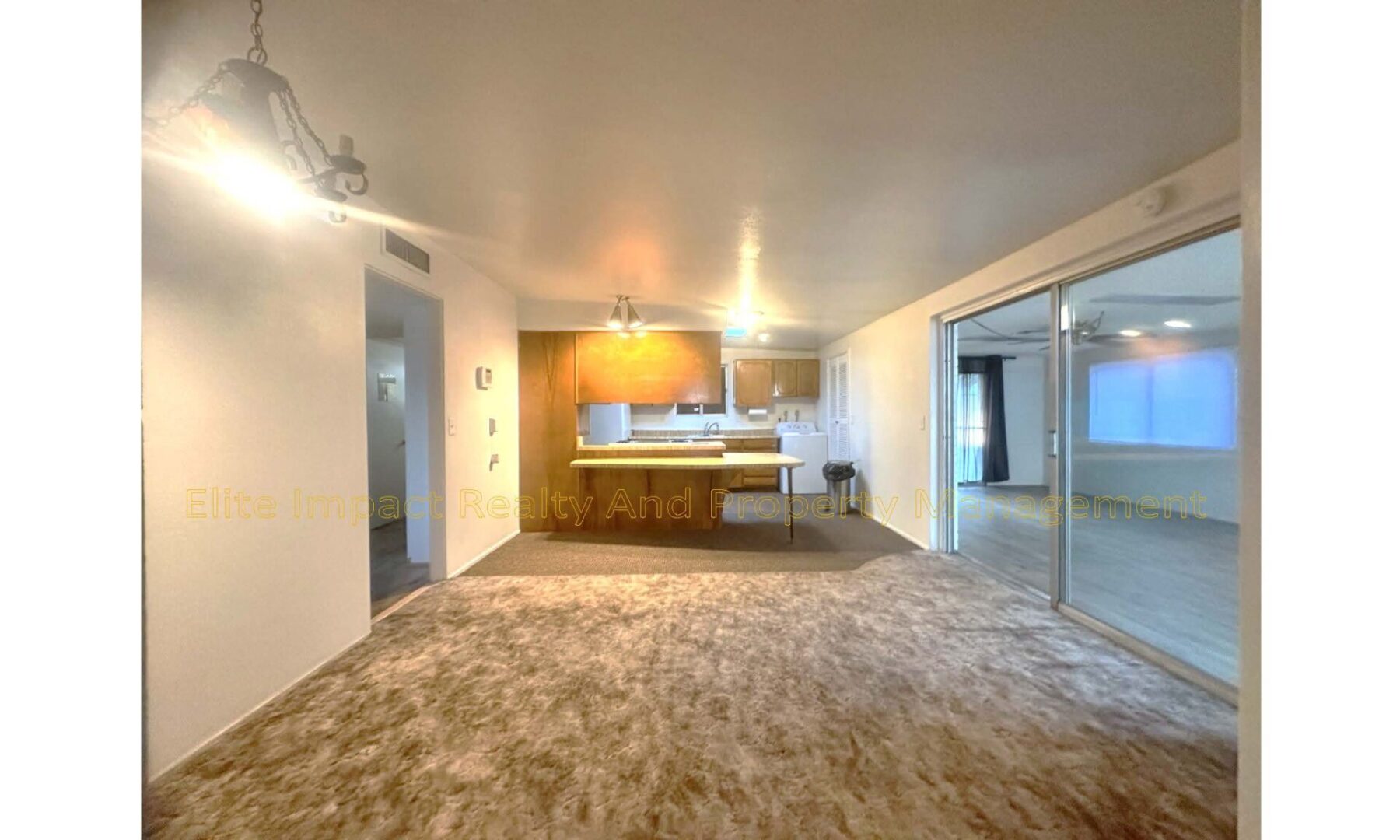 Spacious living room with carpet flooring and open kitchen.