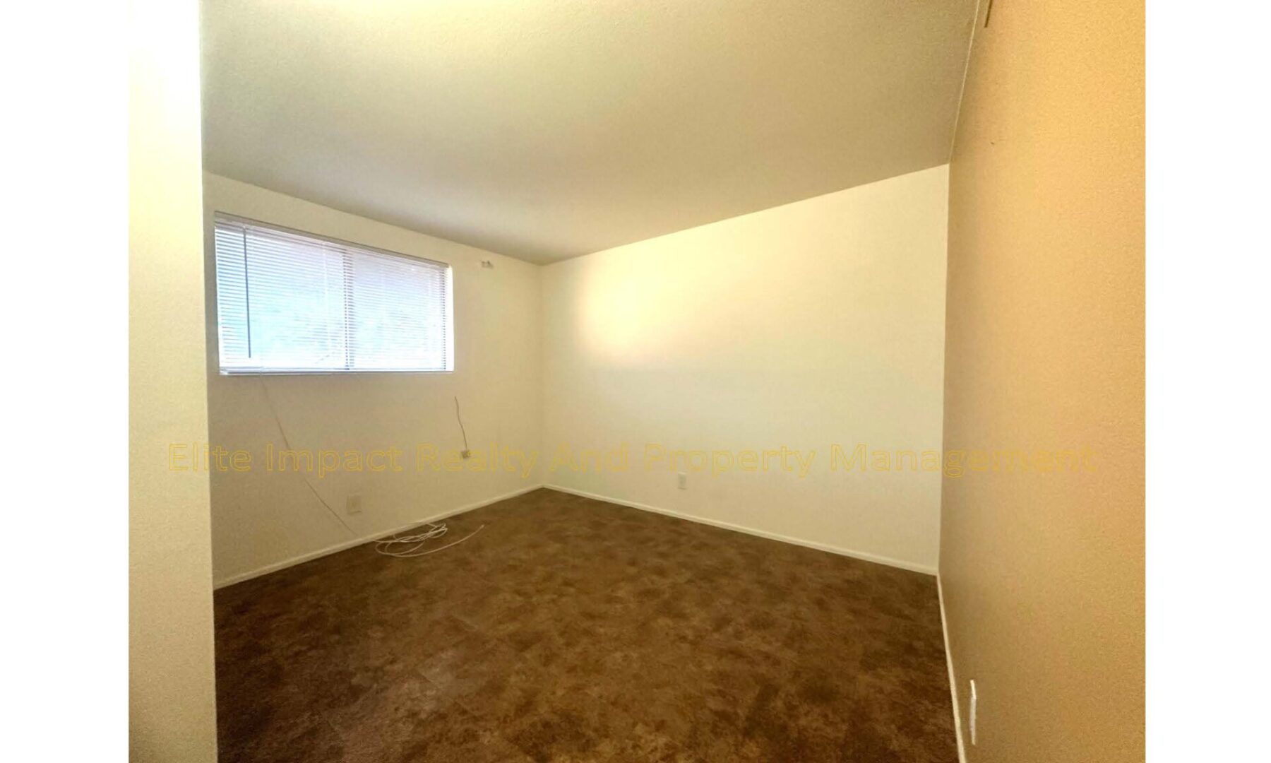 Empty room with beige walls and brown carpet under soft lighting.
