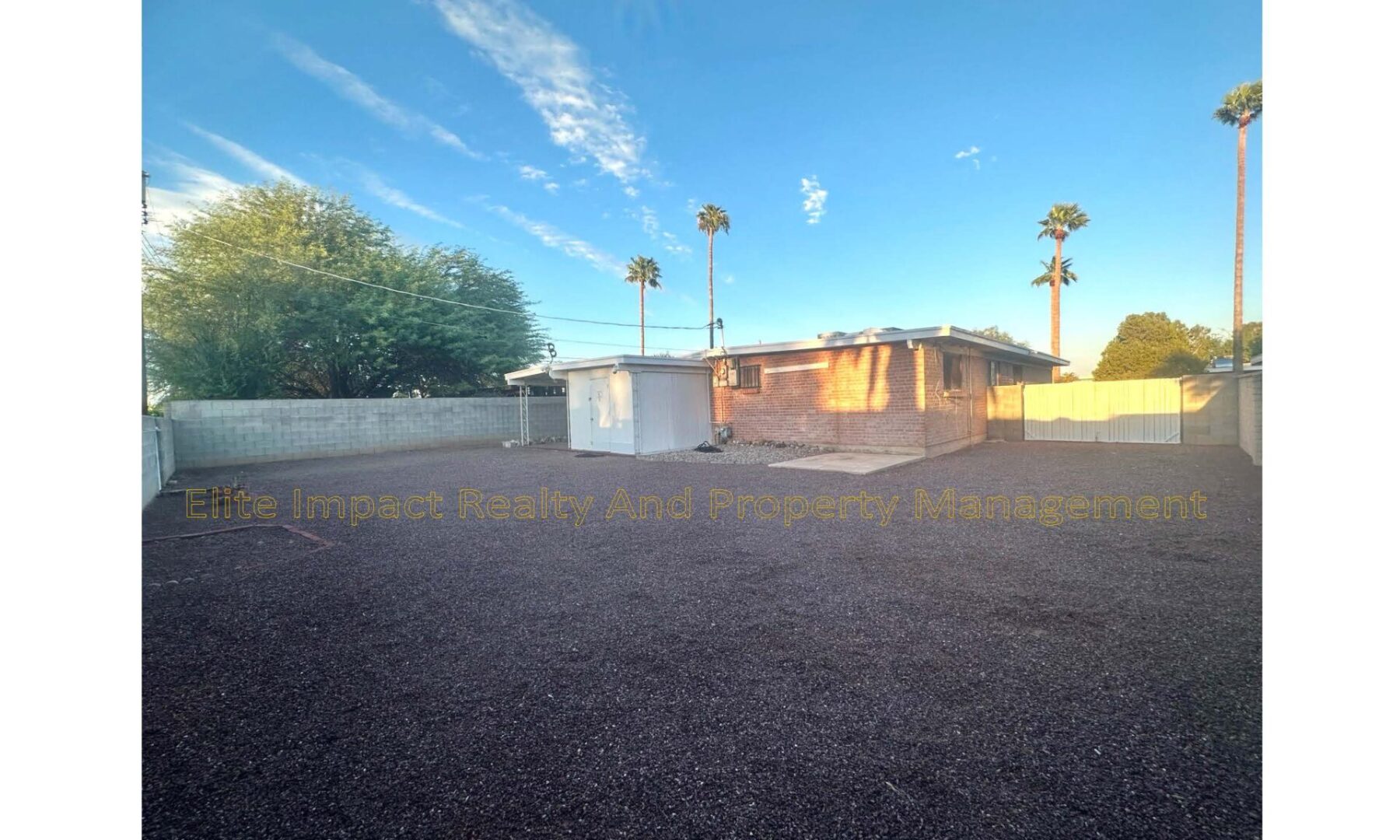 A house with a gravel yard and palm trees under a blue sky.