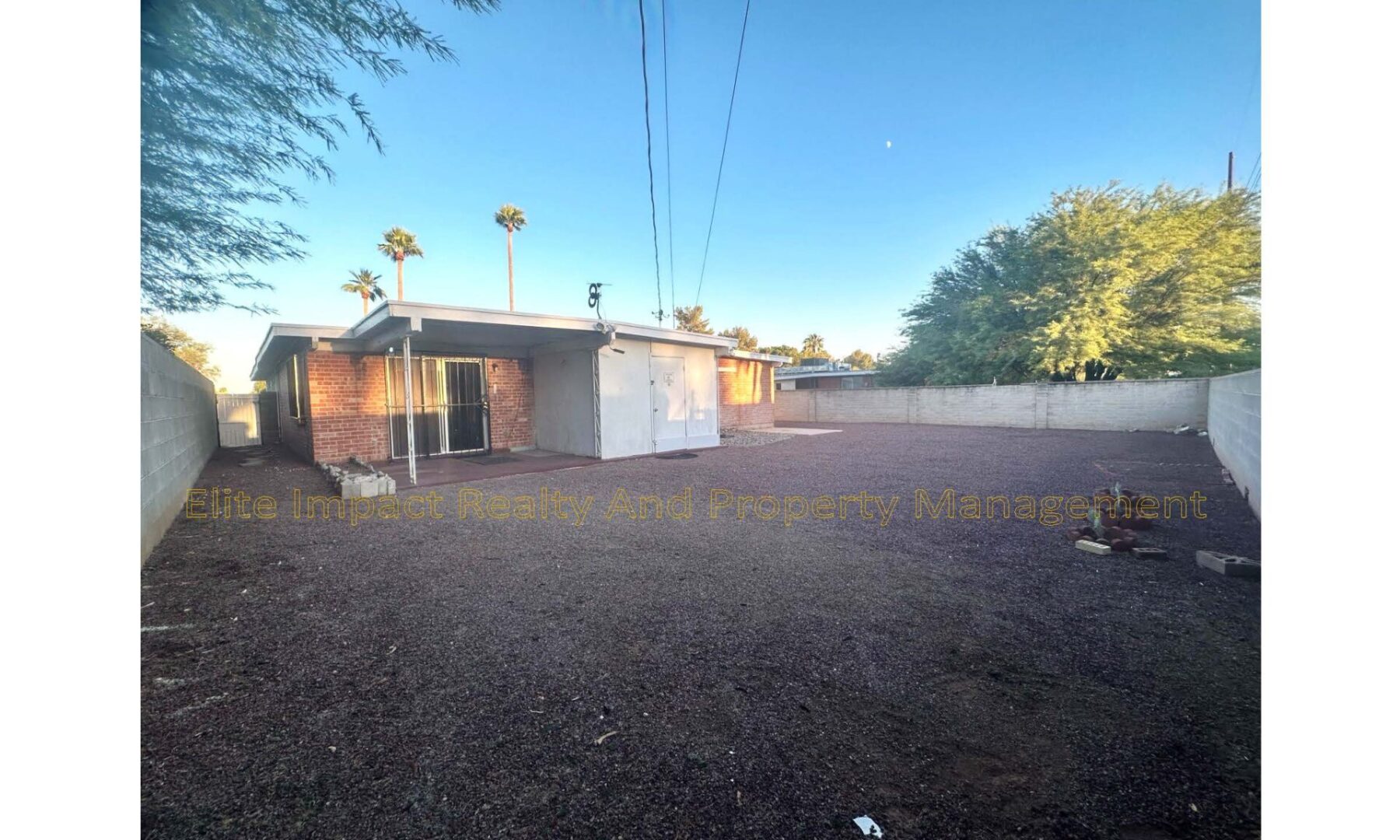 Backyard with a white shed, brick fence, and clear sky at sunset.
