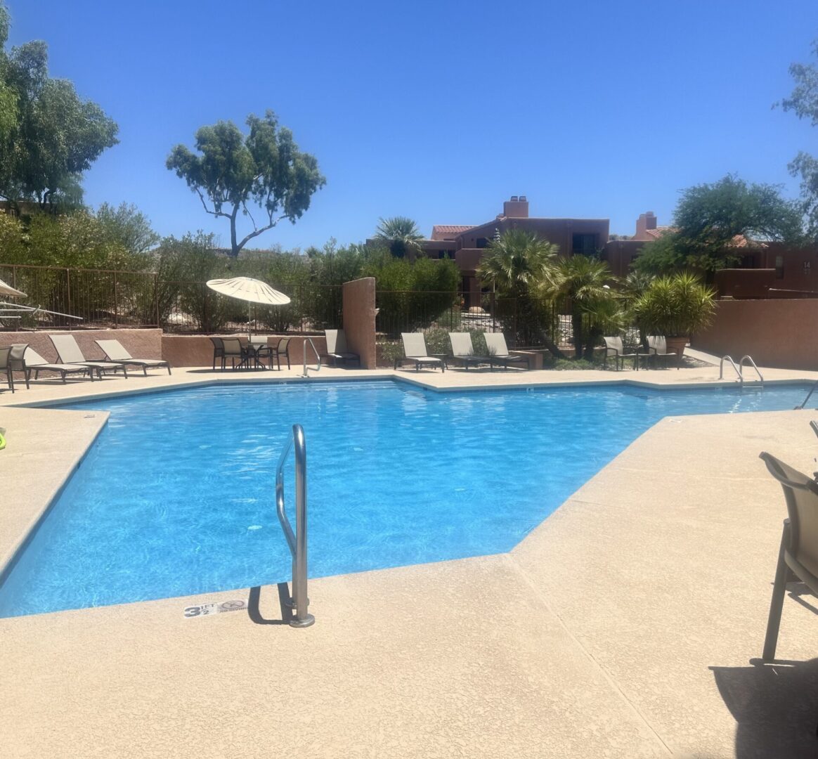 Sunny outdoor pool surrounded by lounge chairs and umbrellas.