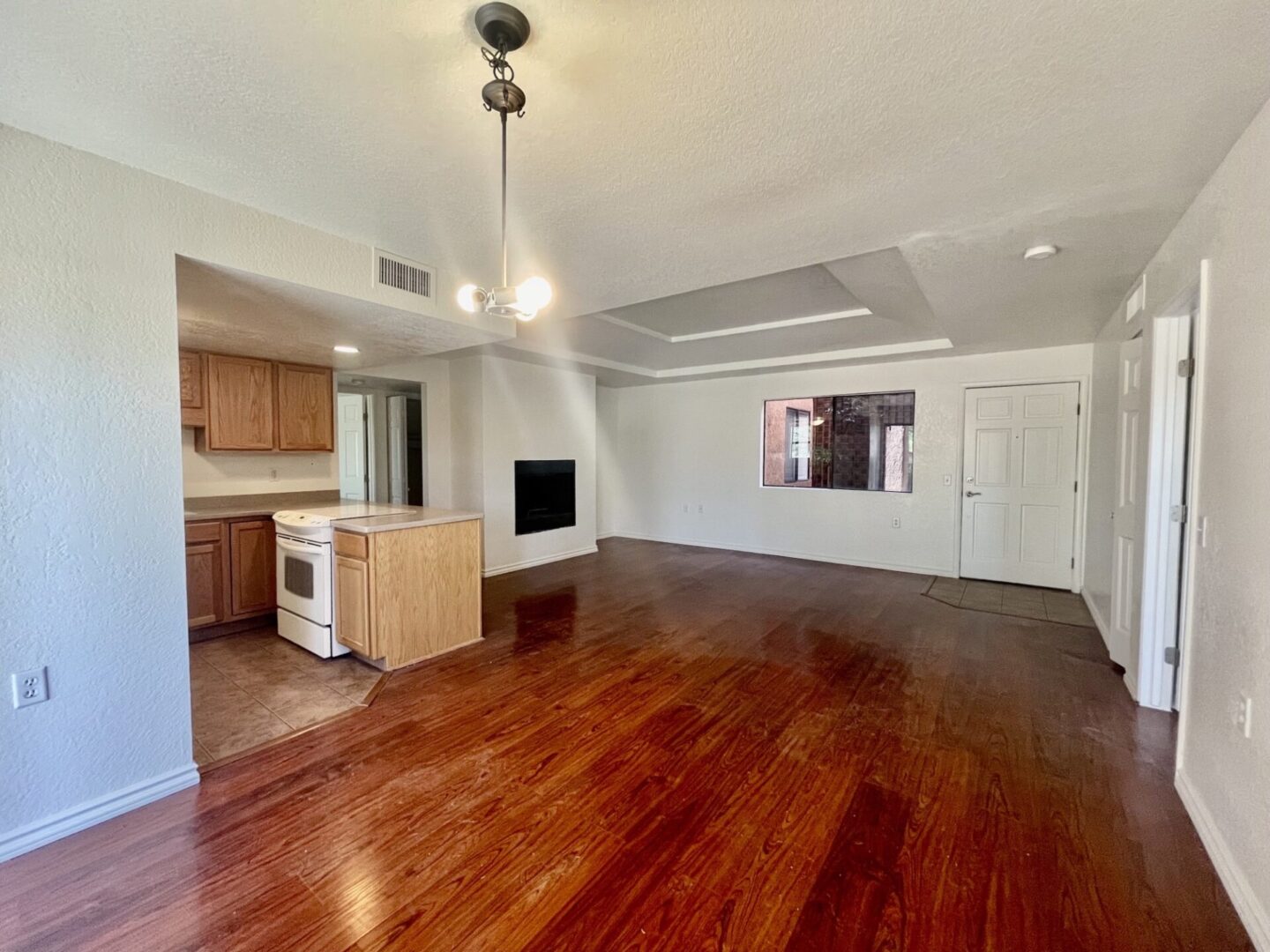 Empty living room with wooden floors and kitchen area.