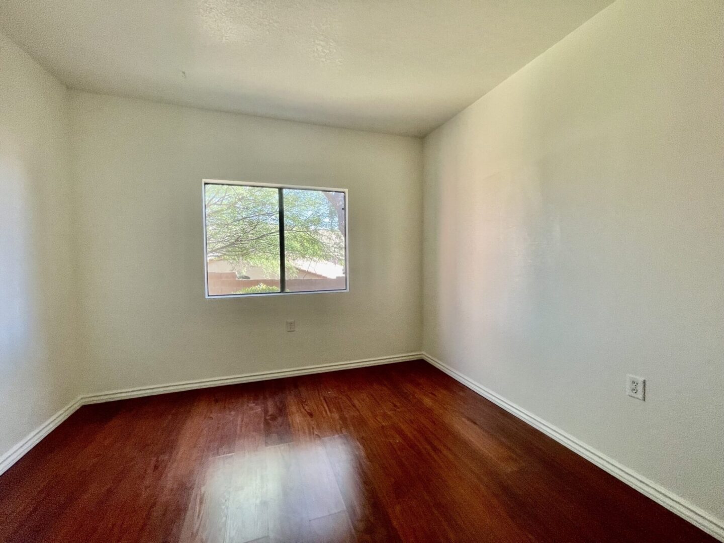 Empty room with wooden floor and window letting in natural light.