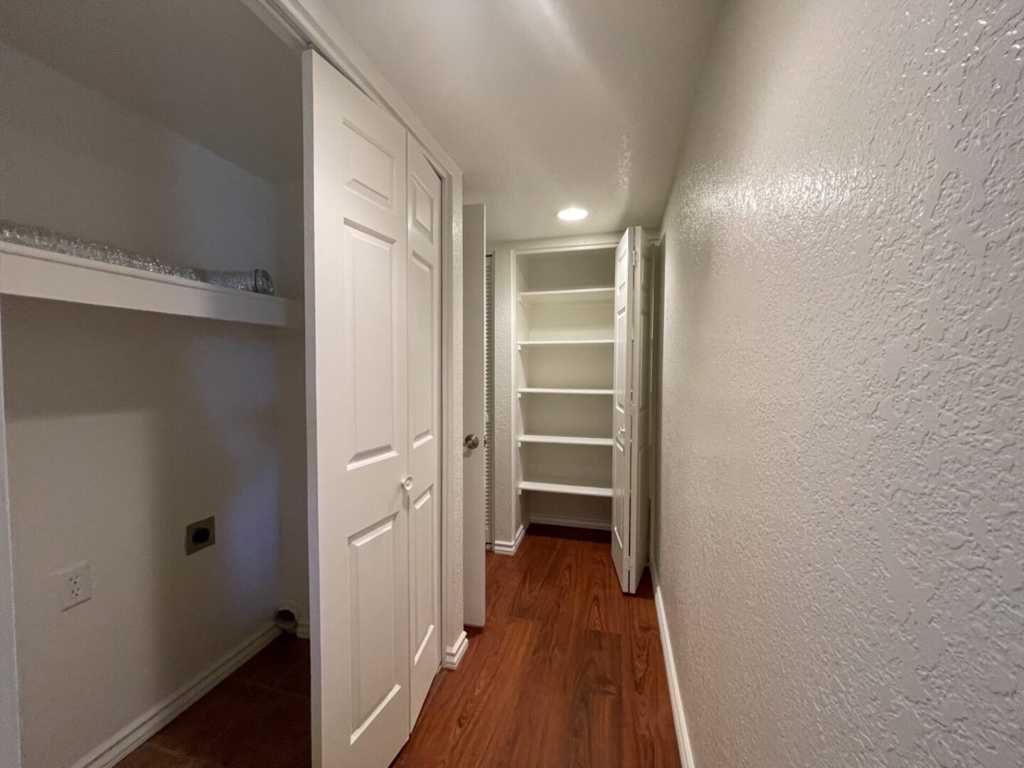 Narrow hallway with wooden floor and built-in shelves at the end.