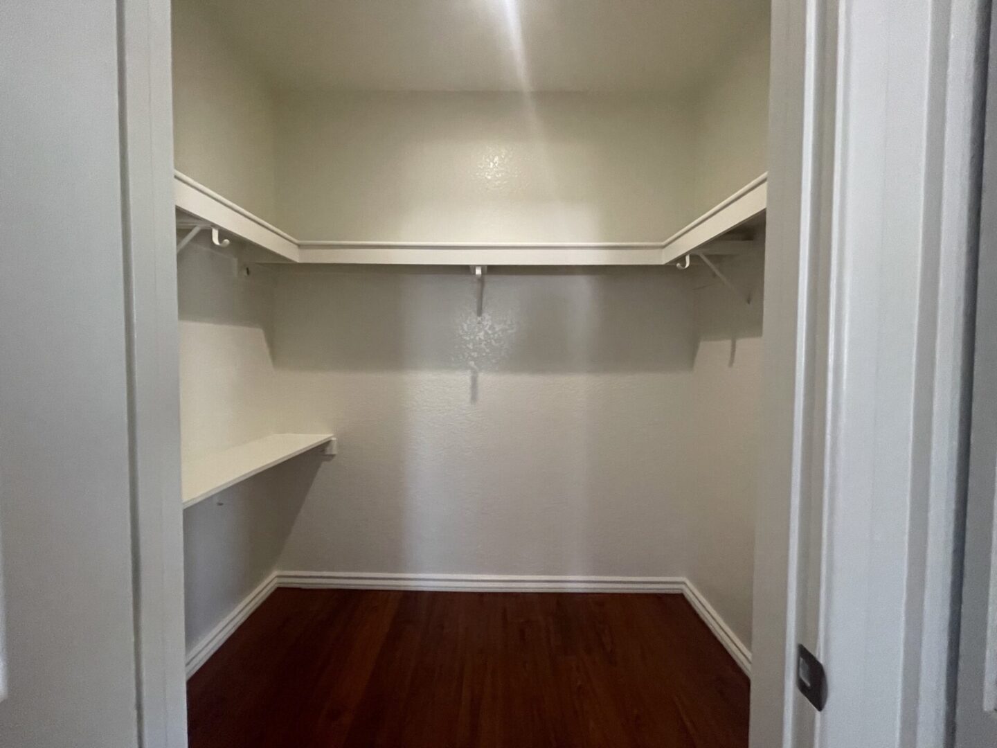 Empty walk-in closet with wooden floor and white shelves.