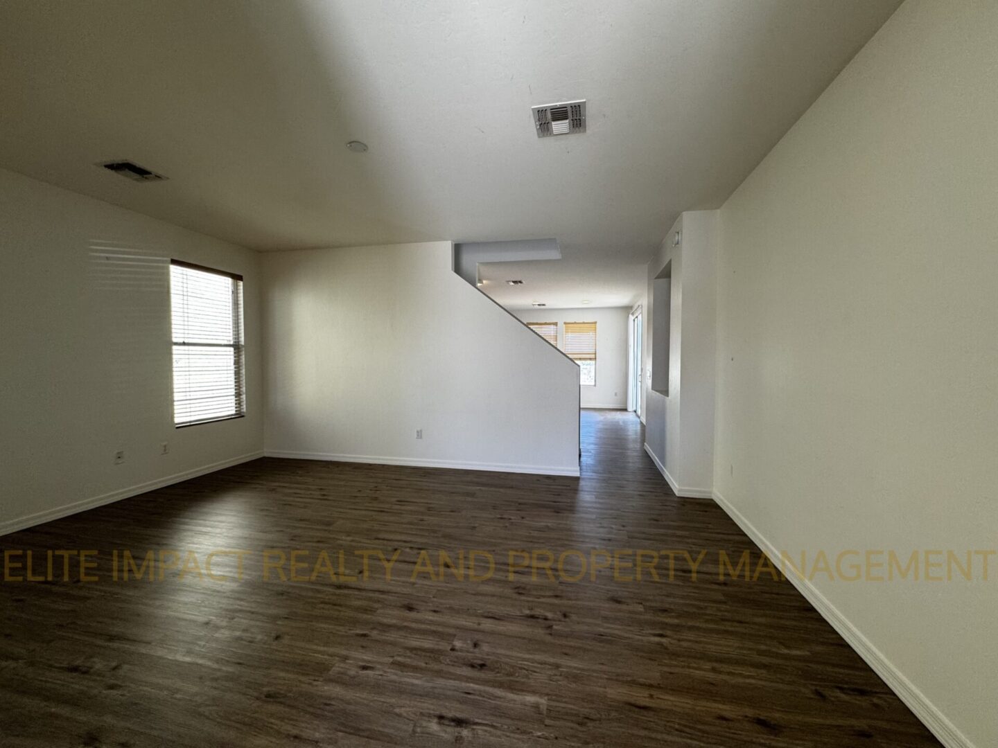 Empty room with wooden floors and white walls, featuring a staircase and natural light from windows.
