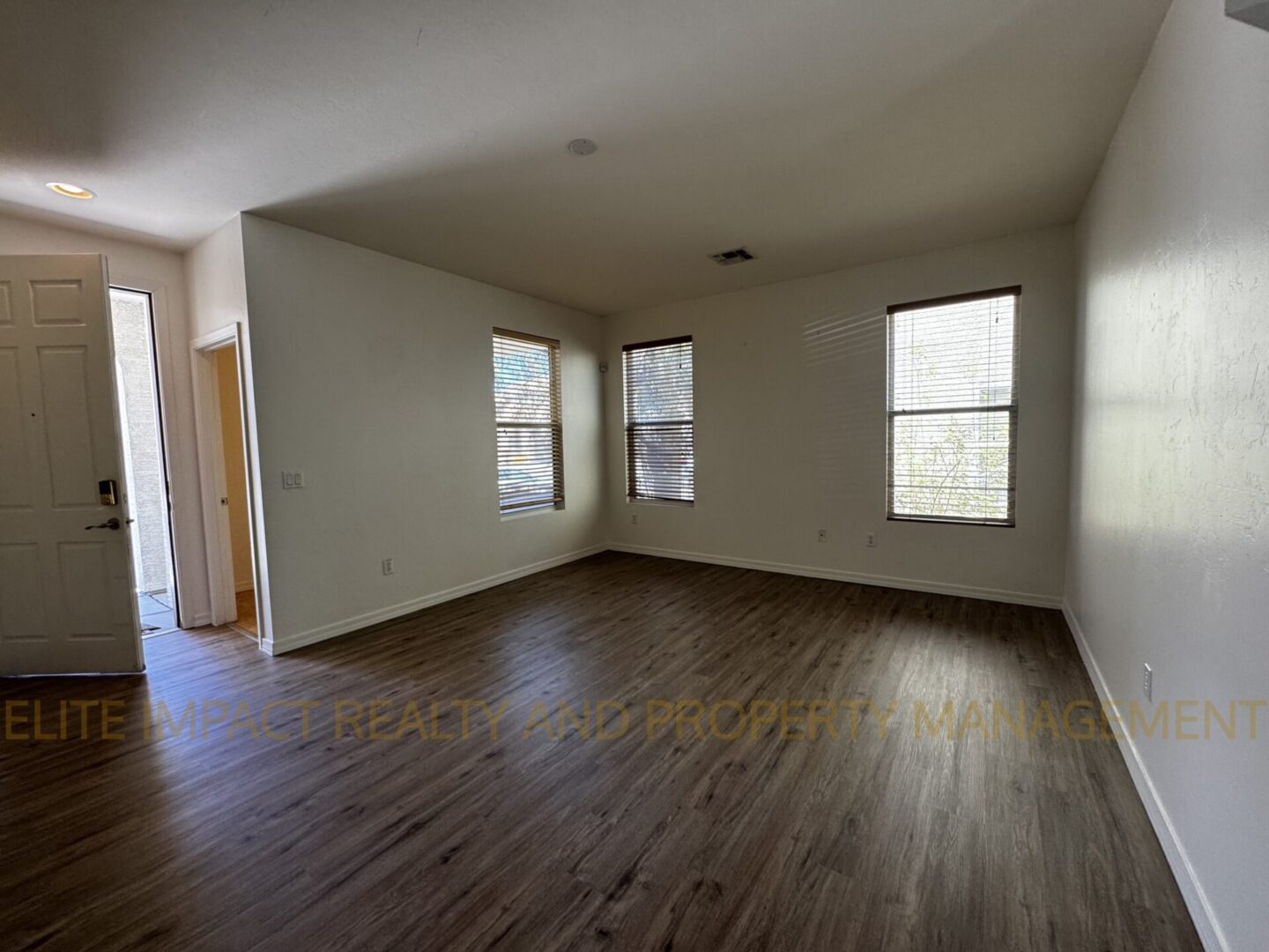 Empty room with hardwood floors and three windows.