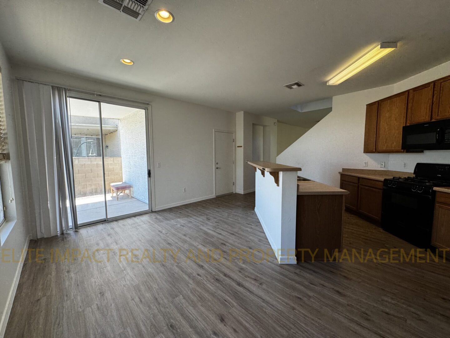Empty living room with sliding glass door and kitchen area.