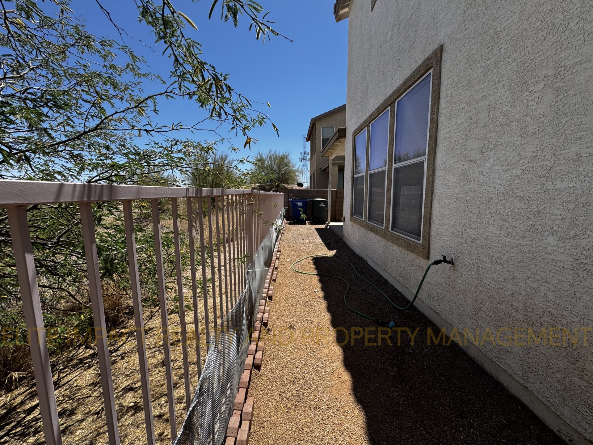Narrow side yard with gravel and metal railing next to a beige house.