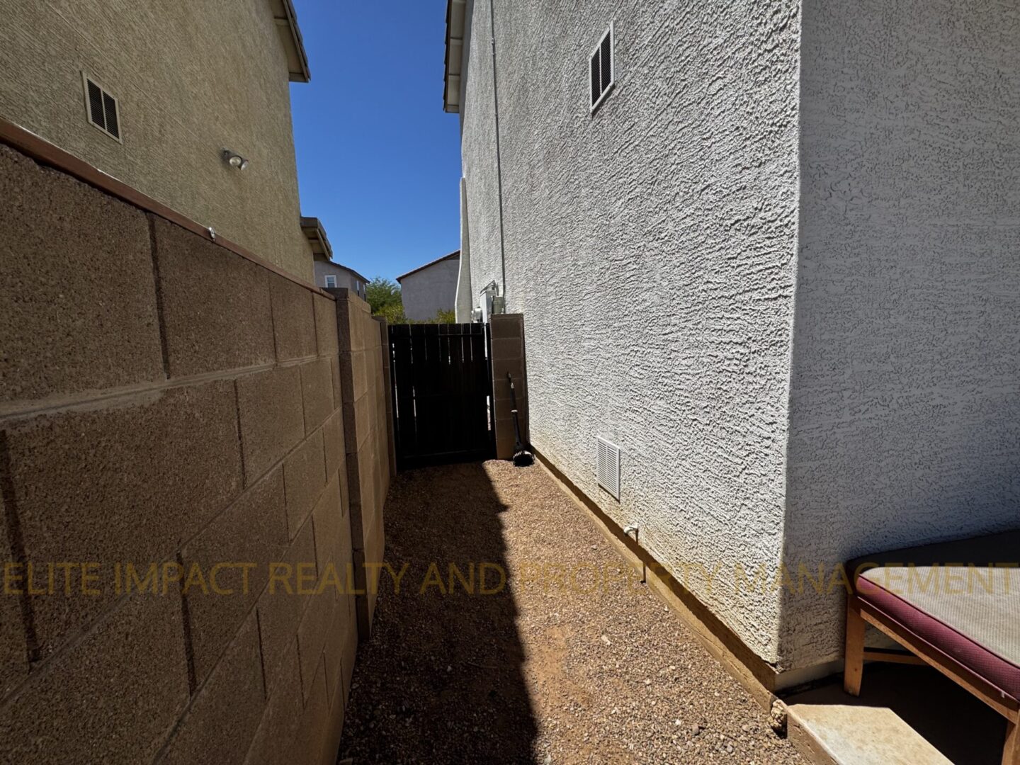Narrow outdoor pathway between two buildings with gravel ground and a wooden gate at the end.