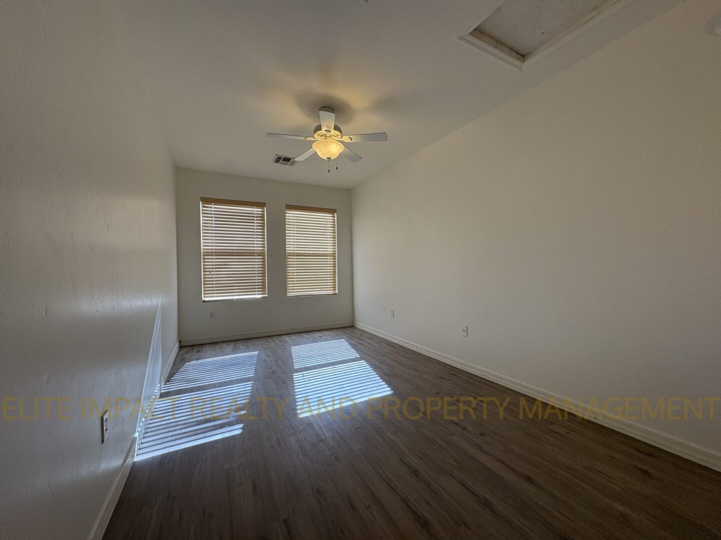 Empty room with wooden floor and ceiling fan under natural light.