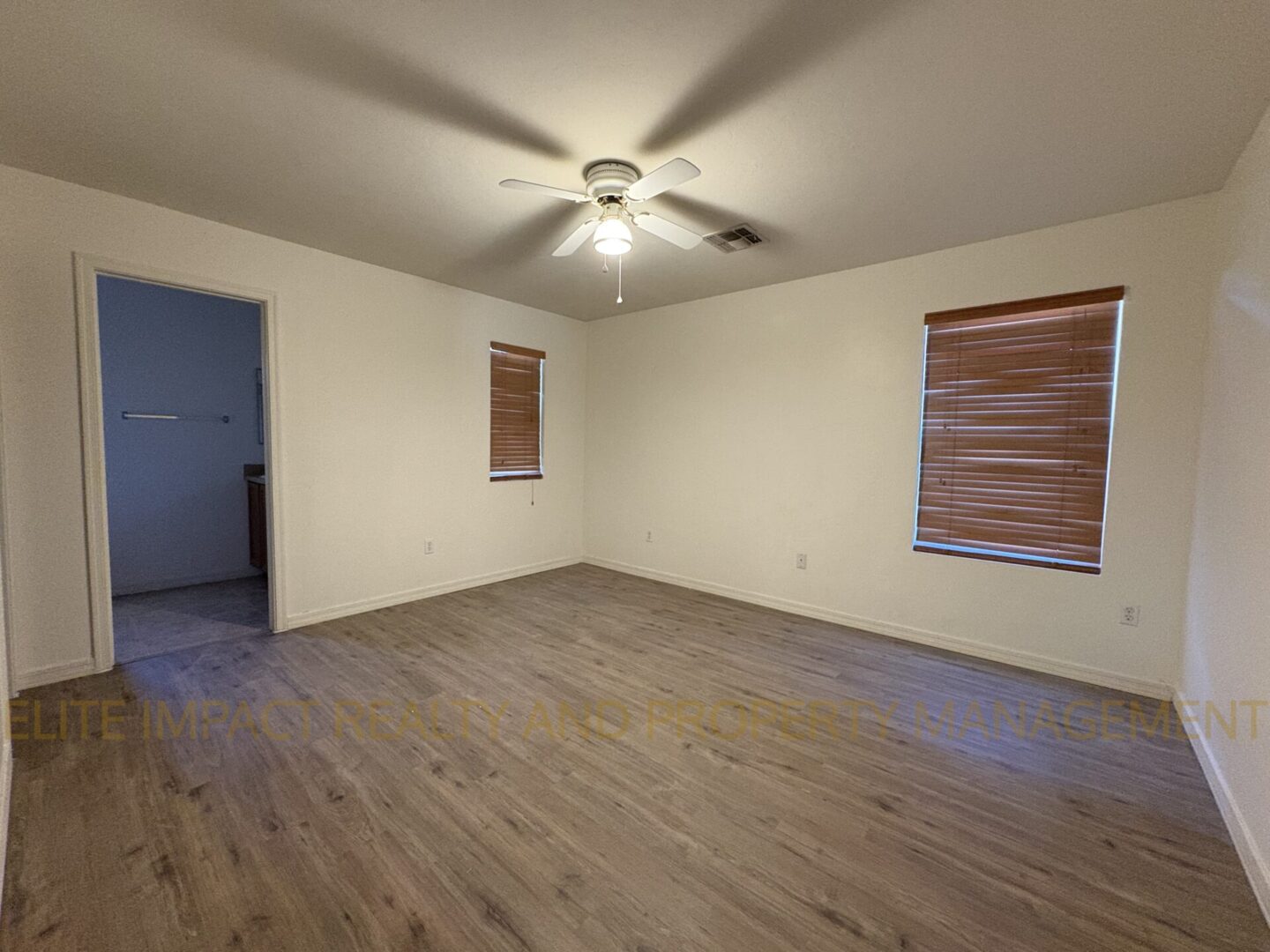 Empty room with wooden flooring, white walls, ceiling fan, and two windows with blinds.