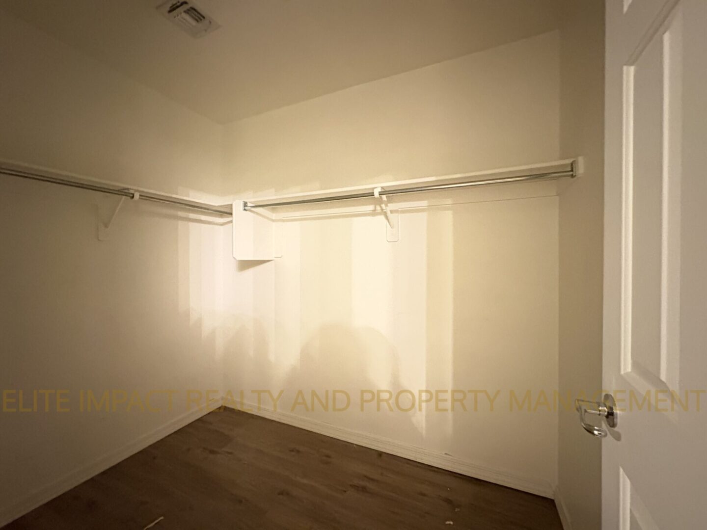 Empty room with wall-mounted closet rods and a hardwood floor.