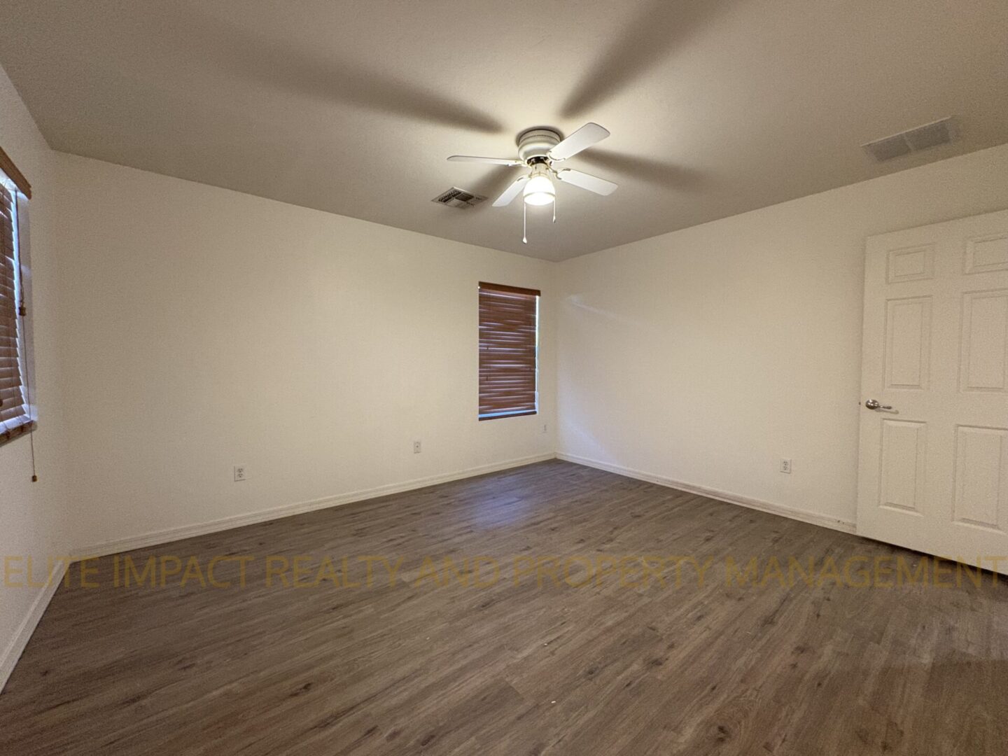 Empty room with wooden flooring and ceiling fan under soft lighting.