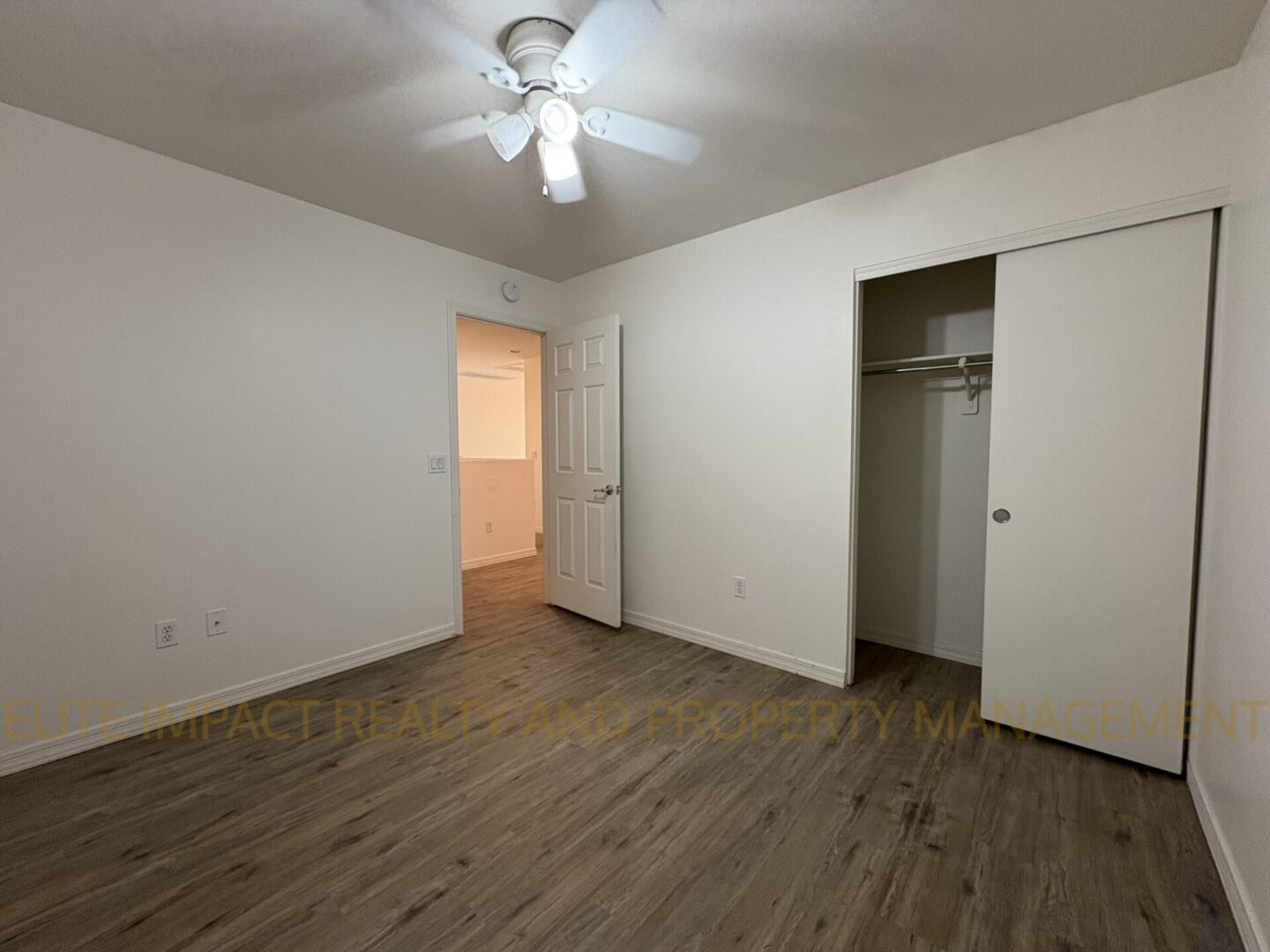 Empty bedroom with wood flooring, ceiling fan, and open closet.