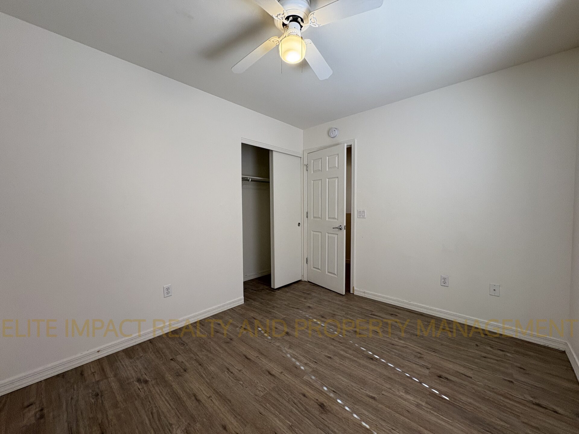 Empty room with wooden floor and ceiling fan.