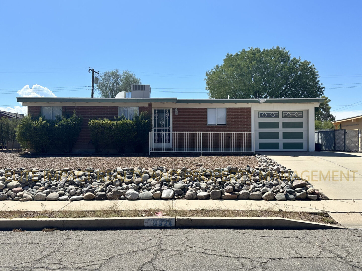 Single-story brick house with a rock garden in front under a clear blue sky.